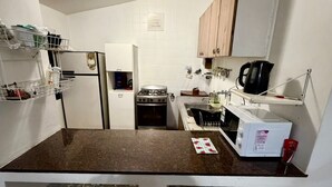 Cocina compacta con estufa a gas, microondas y pileta. Hay alacenas y una mesada con diversos elementos.
