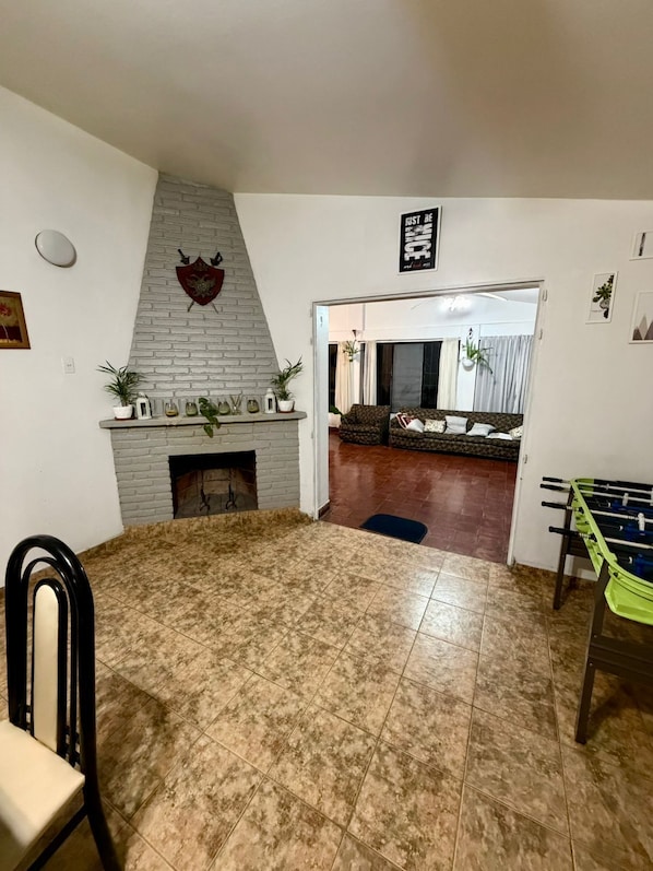Una sala de estar con chimenea, mesa de fútbol y comedor con sillas.