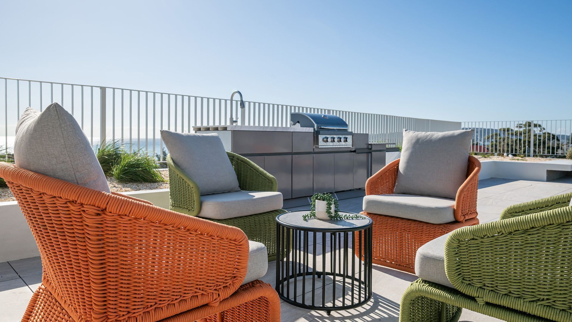 A rooftop patio with wicker furniture, a grill, and a view of the sea.