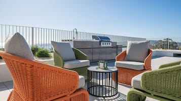 A rooftop patio with wicker furniture, a grill, and a view of the sea.