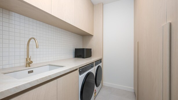 A modern kitchen with a built-in dishwasher, a sink with a gold faucet, and a microwave on the countertop. - Dromana Beach Suites - 104 (Dromana)