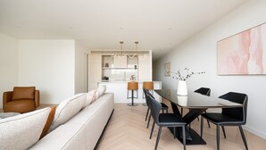 A modern living room with a sofa, a dining table with chairs, and a kitchen area in the background. - Dromana Beach Suites - 104 (Dromana)