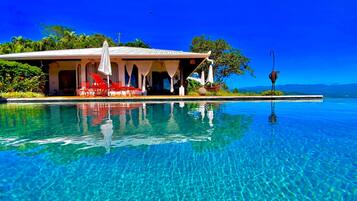 Una piscina cristalina con un área de descanso, sillones rojos y un espacio cubierto para sentarse.