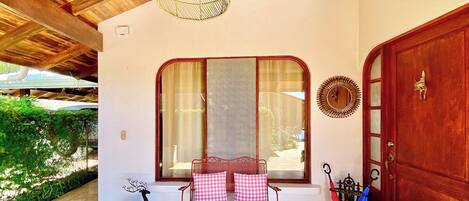 A covered porch with a bench, a wooden door, and a window with curtains.