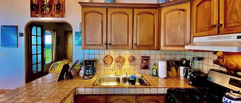 Una cocina con armarios de madera, salpicadero azulejado, estufa y cafetera.