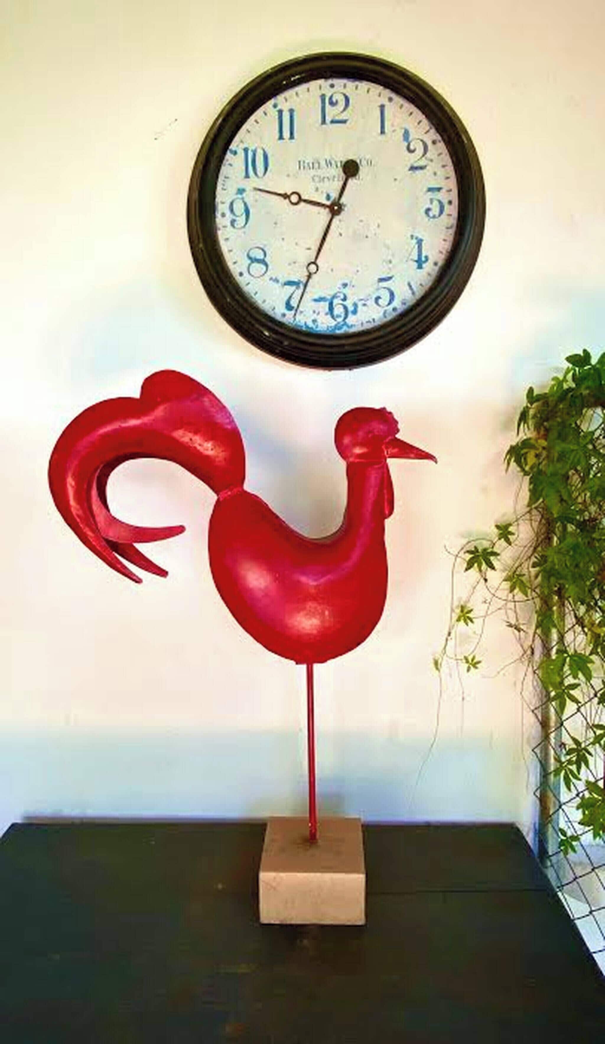 A wall-mounted clock with a rooster sculpture below it.