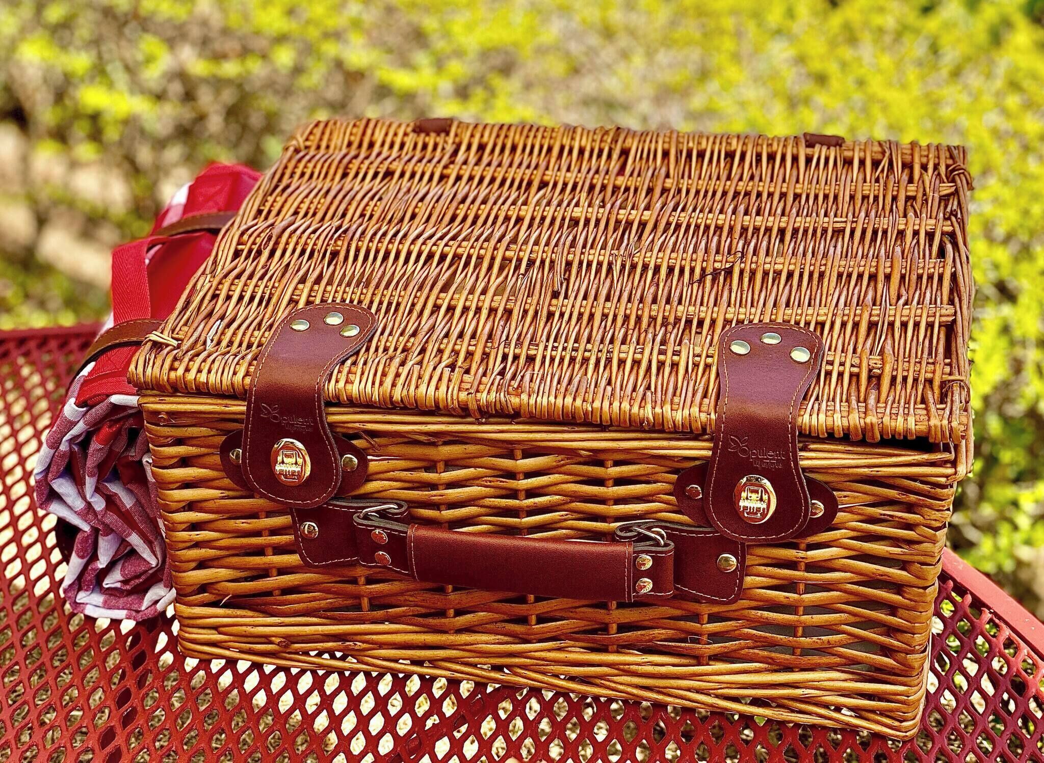 Una cesta de mimbre con correas de cuero y remaches metálicos, sobre una mesa de metal roja.