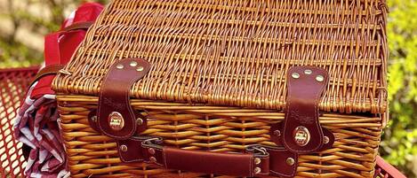 Una cesta de mimbre con correas de cuero y remaches metálicos, sobre una mesa de metal roja.