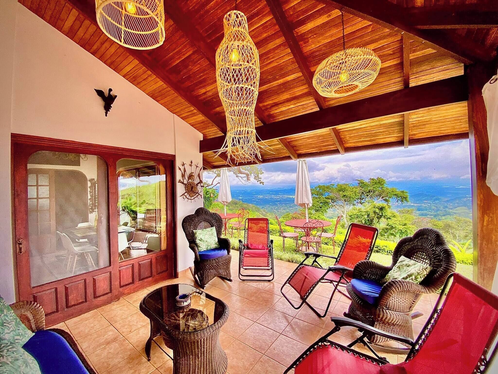 Un patio espacioso con mobiliario de mimbre, una mesa de vidrio y vistas al paisaje.