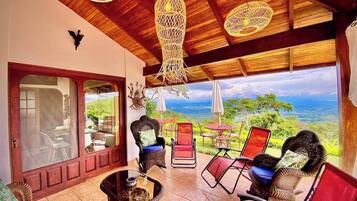 Un patio espacioso con mobiliario de mimbre, una mesa de vidrio y vistas al paisaje.