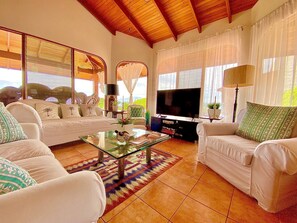 A spacious living room with a large TV, comfortable seating, and a view of the outdoors. - Atenas Villa With Private Infinity Pool and Mountain Views (Jesús)