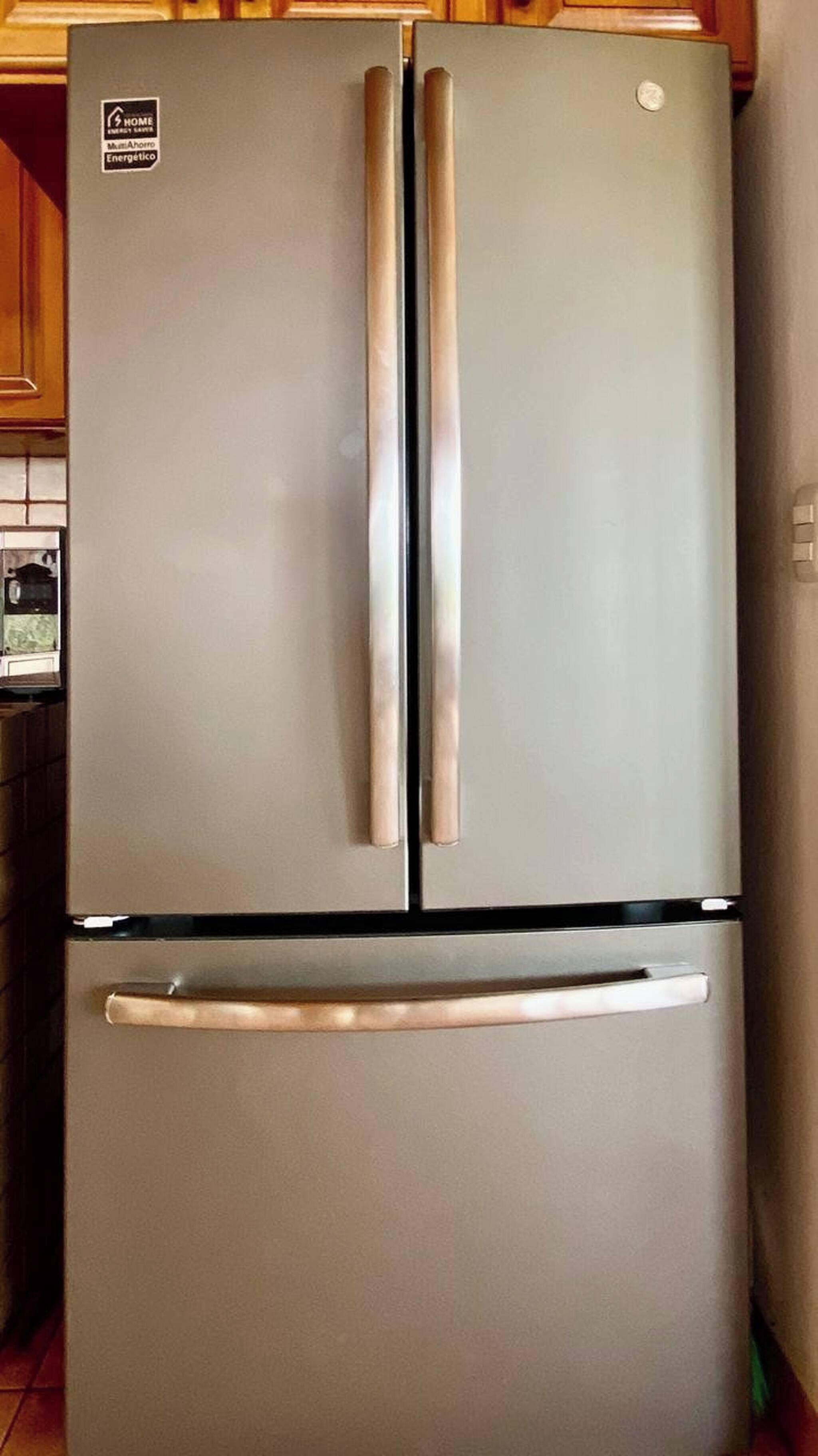 A two-door stainless steel refrigerator with a freezer drawer below, in a kitchen with wooden cabinets.
