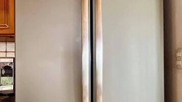 A two-door stainless steel refrigerator with a freezer drawer below, in a kitchen with wooden cabinets.