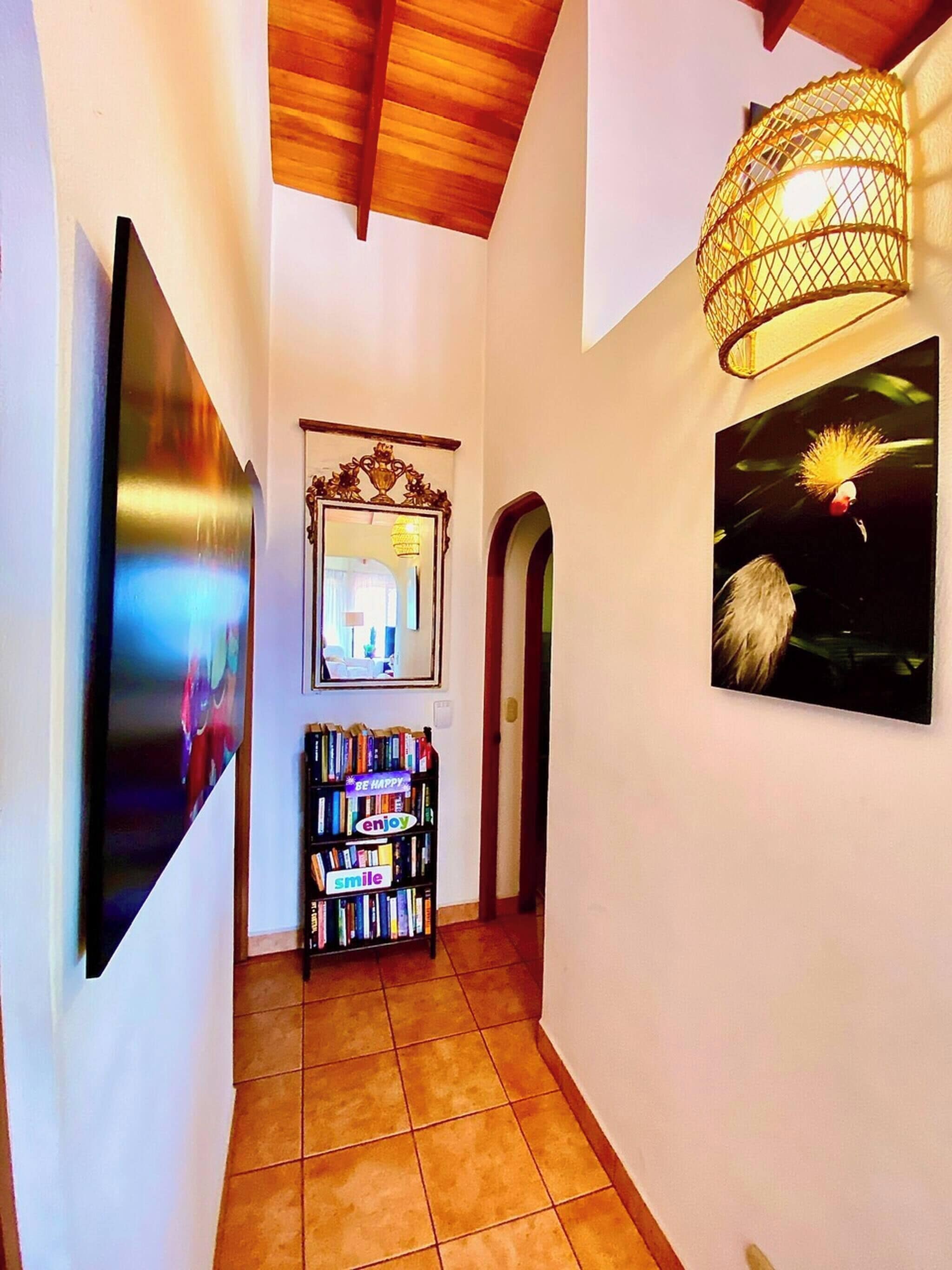 Un pasillo con una estantería, un espejo y un cuadro en la pared.