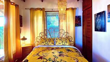 Quarto com cama, ventilador de teto, janela com cortinas e luminária na parede.