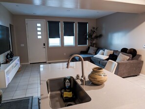 A modern kitchen with a stainless steel sink, a dining area with a white table, and a living room with a grey sofa. - Cozy 2-bedroom condo in charming Rancho Cucamonga (Rancho Cucamonga)