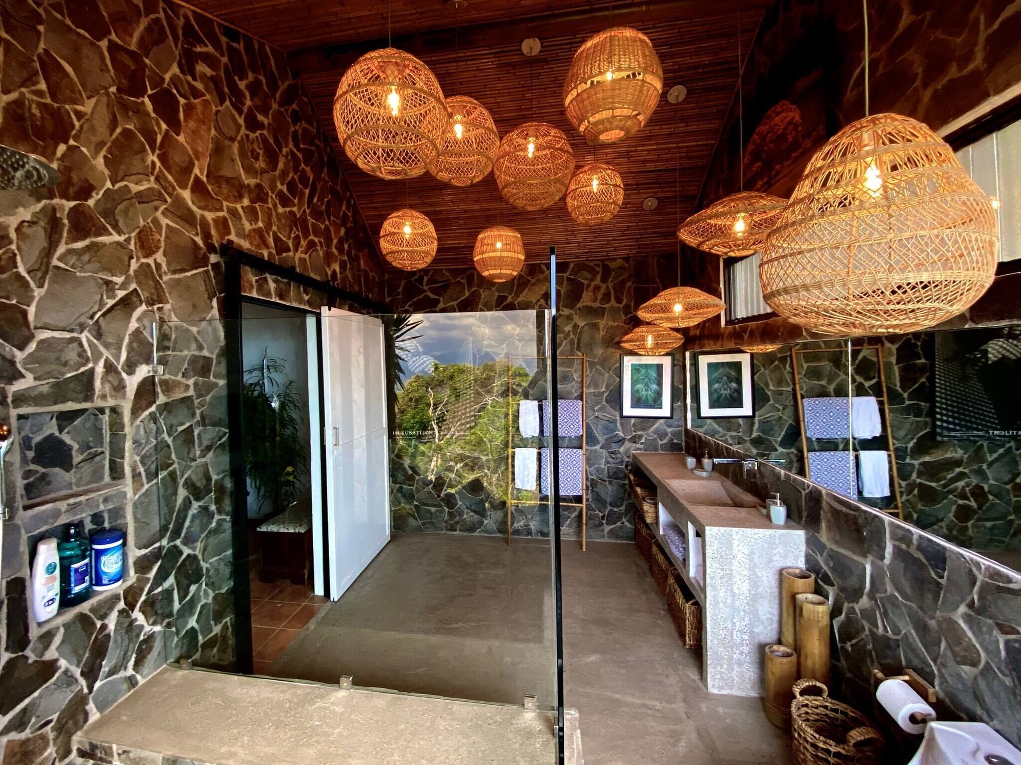 Un baño de paredes de piedra con un espejo grande, un lavamanos y una zona de ducha.