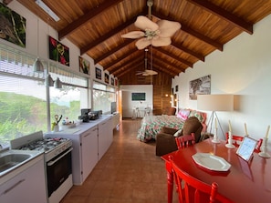 Una cocina amplia con estufa a gas, un comedor con mesa roja y un ventilador de techo.