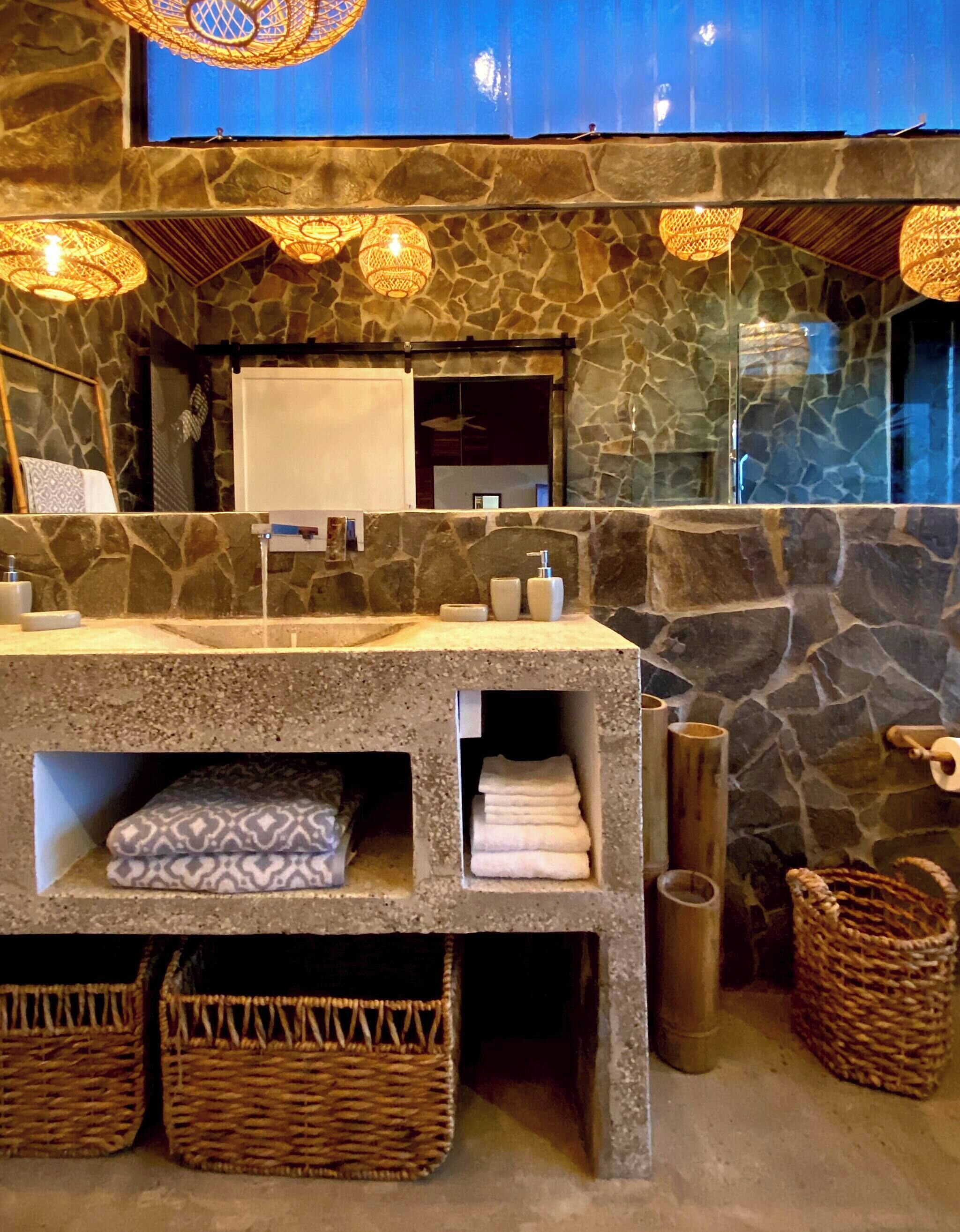 A bathroom with a stone wall, a sink with soap dispensers, a towel rack, and wicker baskets.