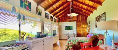 Une cuisine équipée d’une cuisinière à gaz, un coin repas avec une table rouge et un ventilateur de plafond.