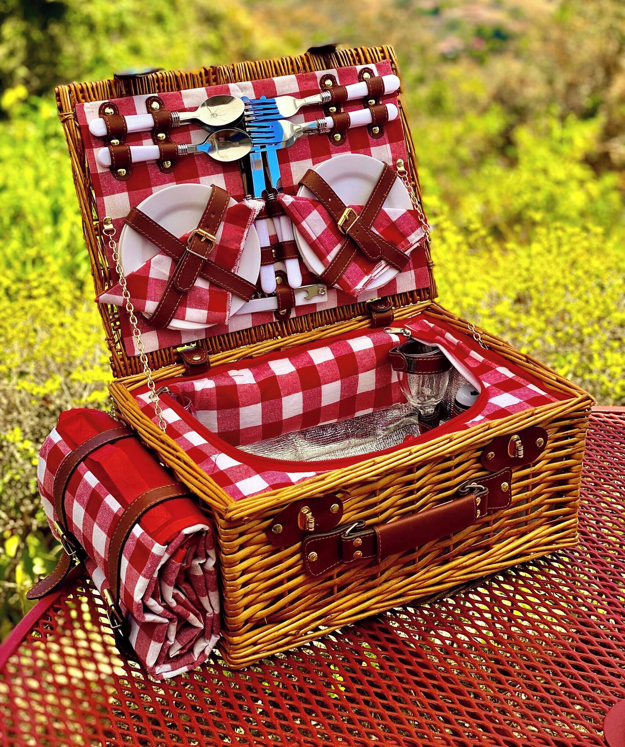 Un panier de pique-nique en osier, avec un tissu à carreaux comme doublure, un torchon enroulé et une tasse en métal.