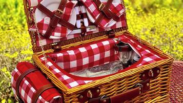 Un panier de pique-nique en osier, avec un tissu à carreaux comme doublure, un torchon enroulé et une tasse en métal.
