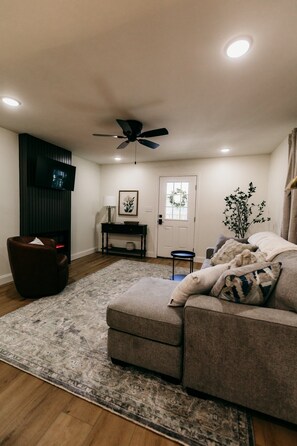 A living room with a sofa, a television, a ceiling fan, and a door.