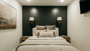 A bedroom with a bed, a ceiling fan, two bedside lamps, a mounted TV, and a bench. - NEW Luxury Carriage House Downtown Somerset (Somerset)