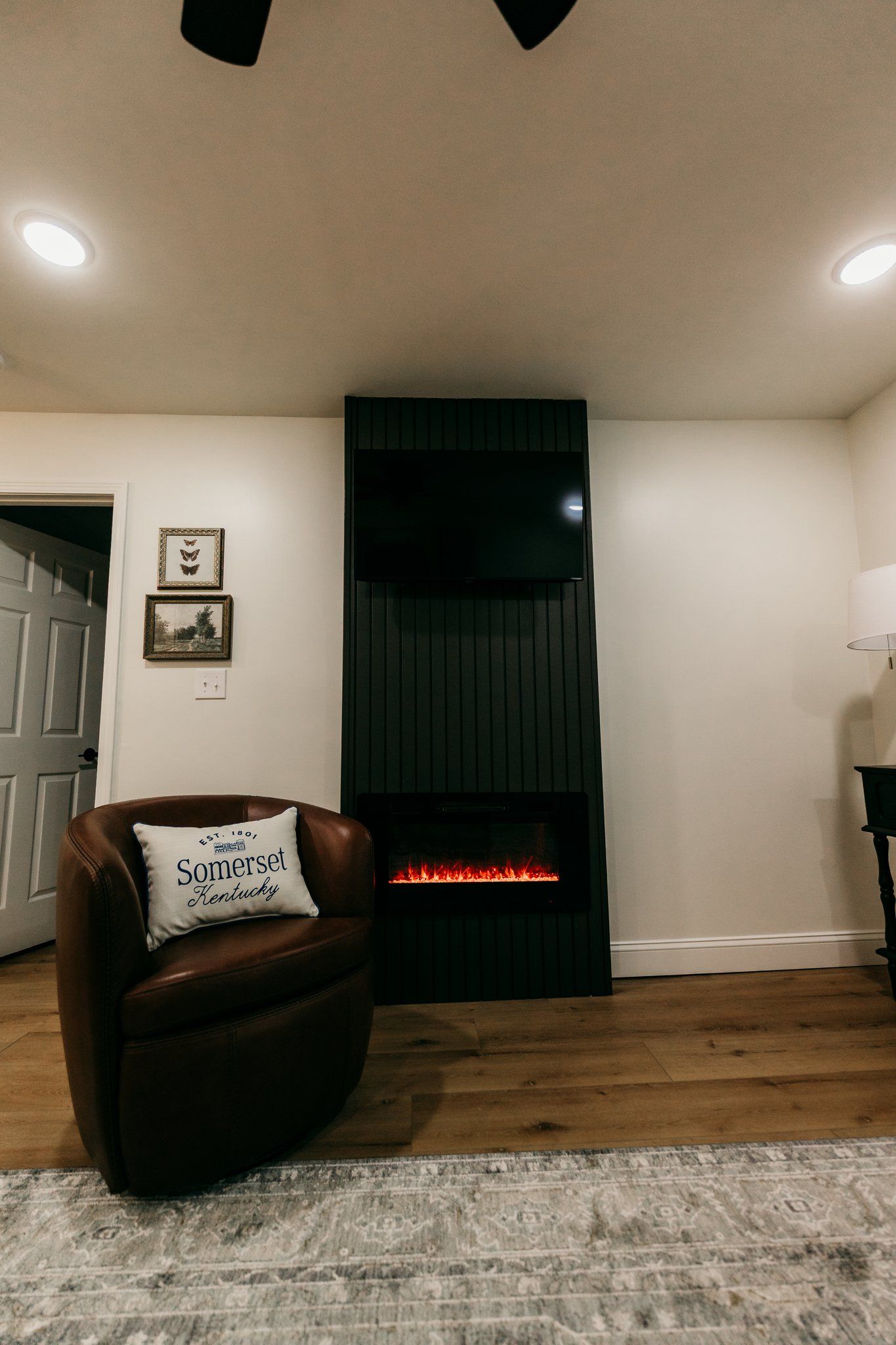A living room with a leather armchair, a fireplace, a rug, and a door.