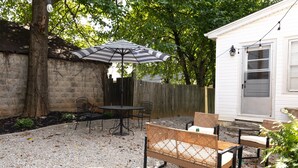 A backyard patio with a table and chairs, a striped umbrella, and a wooden fence. - NEW Luxury Carriage House Downtown Somerset (Somerset)