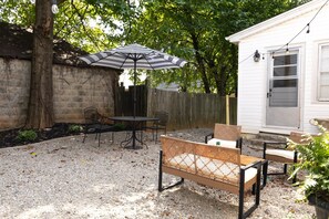 Ein Hinterhof mit einer Terrasse, einem Tisch, Stühlen, einem gestreiften Sonnenschirm und einem Holzzaun.