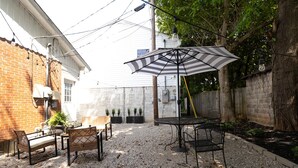 An outdoor patio with a table and chairs, a striped umbrella, and a brick wall. - NEW Luxury Carriage House Downtown Somerset (Somerset)