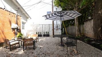Eine Terrasse im Freien mit Tisch und Stühlen, einem gestreiften Sonnenschirm und einer Ziegelwand.