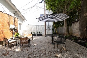 Eine Terrasse im Freien mit Tisch und Stühlen, einem gestreiften Sonnenschirm und einer Ziegelwand.