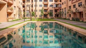 Ein modernes Wohngebäude mit einem zentral gelegenen Schwimmbecken, umgeben von Grünflächen und einem gepflegten Rasen.
