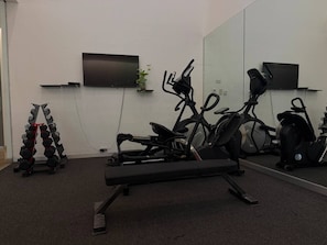Ein Fitnessraum mit Trainingsgeräten, einem Fernseher und einer Pflanze.