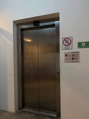Geschlossene Lift-Tür mit einem Rauchverbotsschild und einem Poster für das Wellness-Center an der Wand.