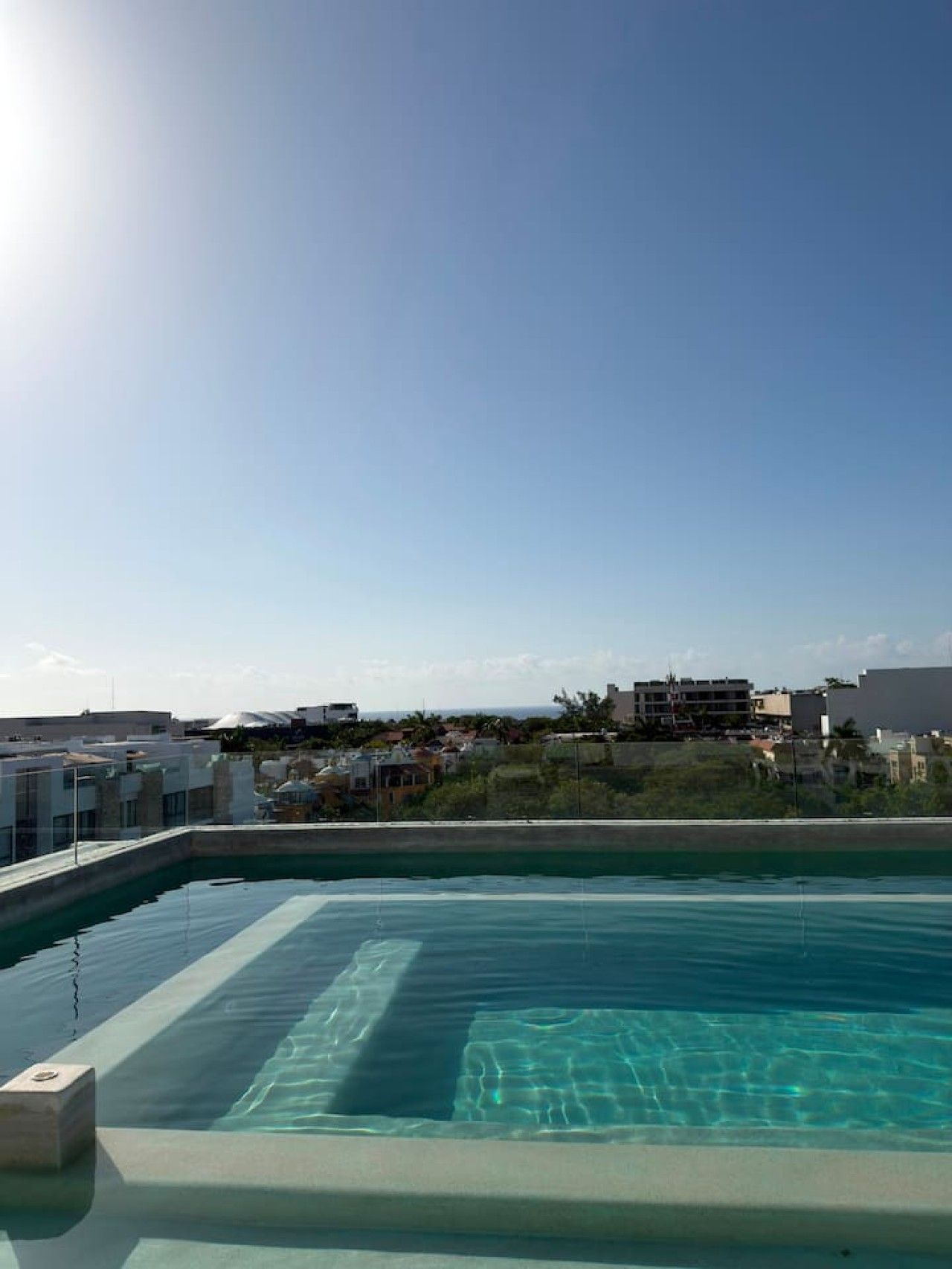 A rooftop swimming pool with clear blue water, surrounded by buildings and a clear sky.