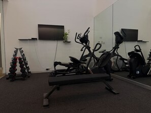 Ein Fitnessraum mit Trainingsgeräten, einem Fernseher und einer Pflanze.