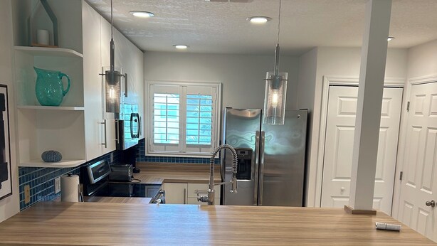 A modern kitchen with a central island, bar stools, a refrigerator, and pendant lighting. - Cozy 2-bed/2 bath condo in Saddlebrook Resort (Zephyrhills)