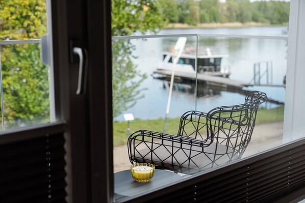 A window with a view of a lake, a boat docked, and a metal chair with a candle on the windowsill.