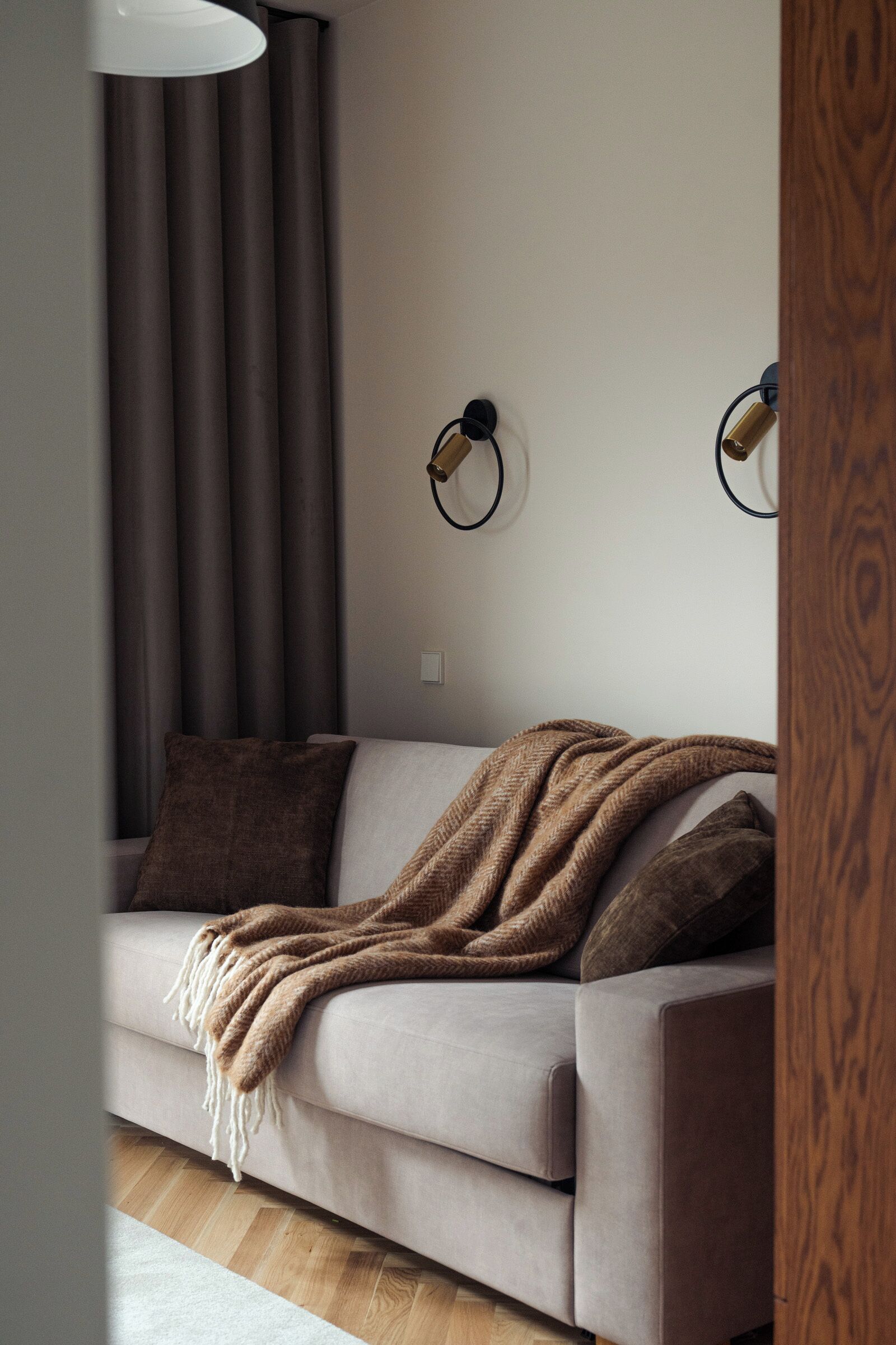 A modern living room with a sofa, a throw blanket, and a wall-mounted lamp.