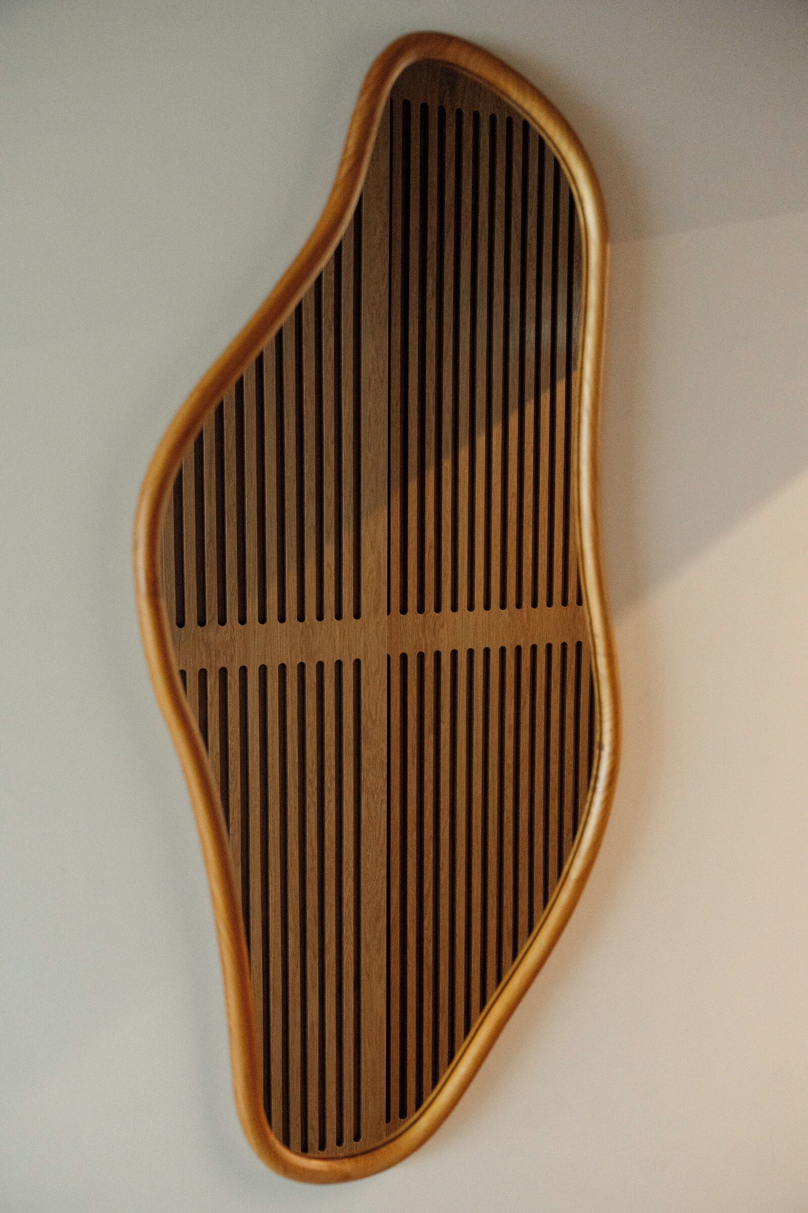 A wall-mounted, wooden, oval-shaped object with vertical slats.