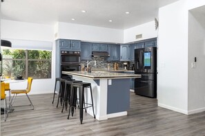 A modern kitchen with a central island, bar stools, and a dining area with a yellow chair. - King Palm|Amazing Pool • Game Room • Near Kierland (Scottsdale)