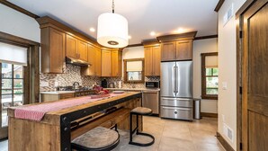 A modern kitchen with wooden cabinets, a central island with stools, stainless steel appliances, and a pendant light.