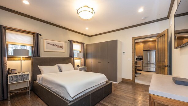 A modern bedroom with a large bed, bedside tables, a desk, and a view into the kitchen.