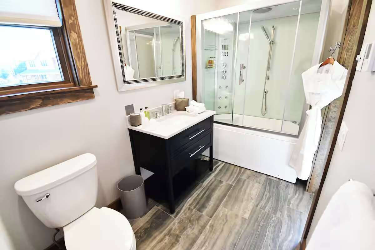 Un baño moderno con inodoro, lavamanos, espejo y ducha con mampara de vidrio.