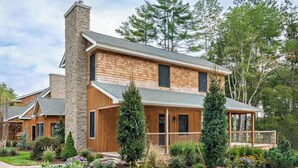 A two-story house with a stone chimney, wooden siding, and a well-maintained garden with various plants and flowers.