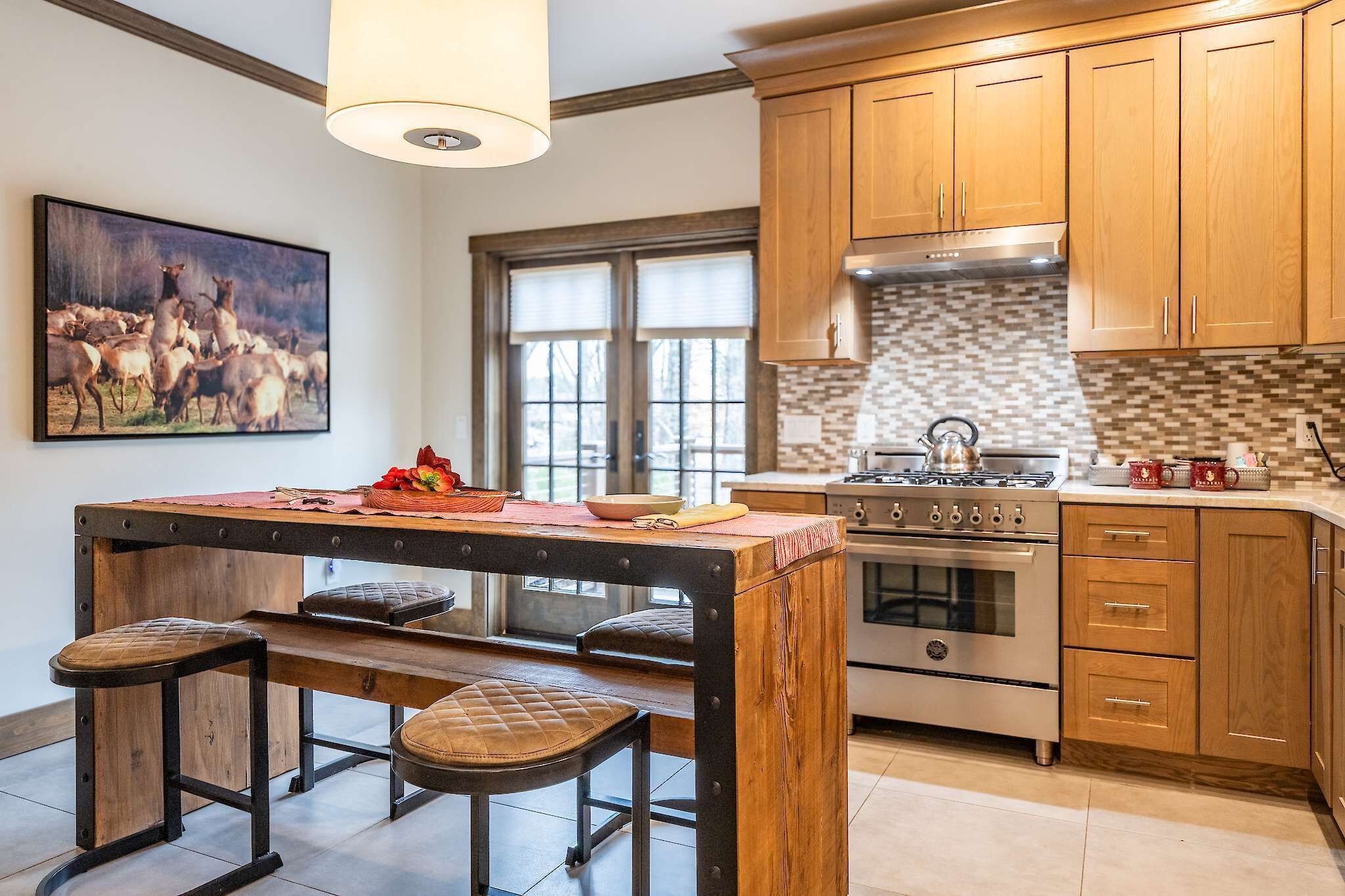 A kitchen with wooden cabinets, a central island with stools, a stove, and a large window.