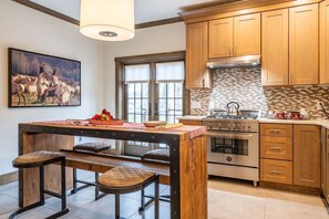 A kitchen with wooden cabinets, a central island with stools, a stove, and a large window.